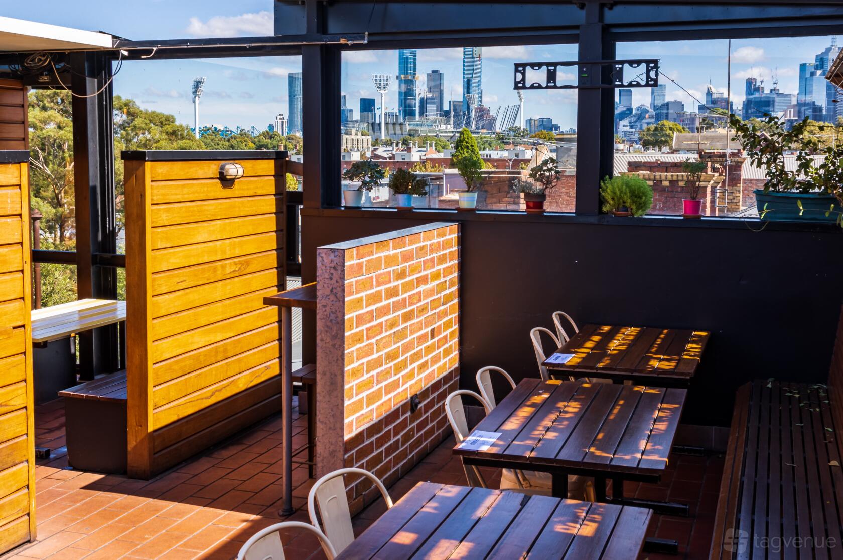 A rooftop pub with wooden tables, brick partitions, and city skyline views at Mt View Hotel.