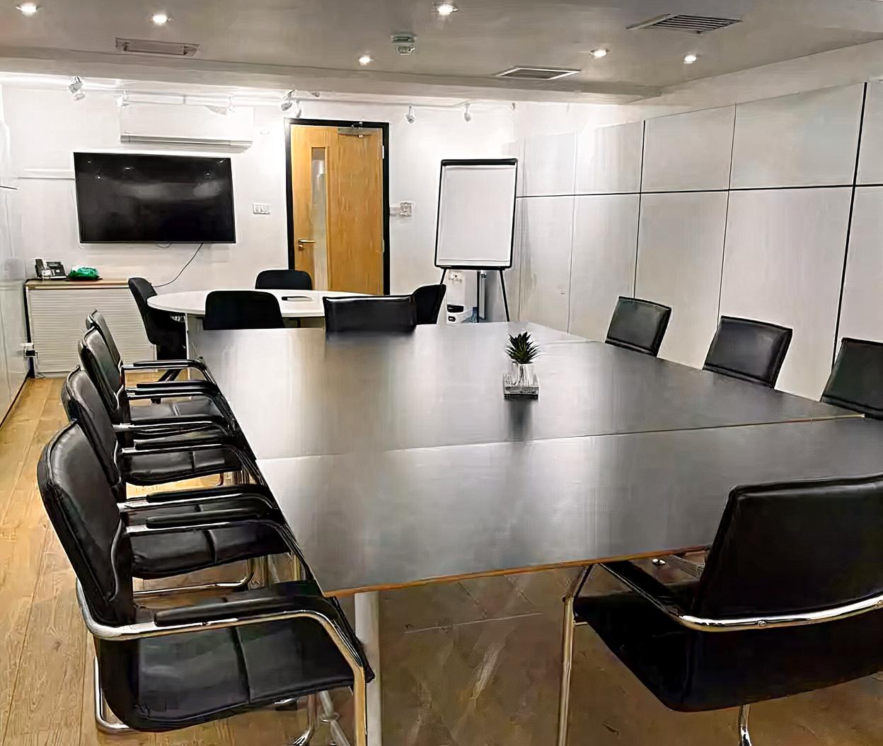 A boardroom with a large black conference table, black chairs, wall-mounted TV, and flip chart at Whitefriars Bristol.