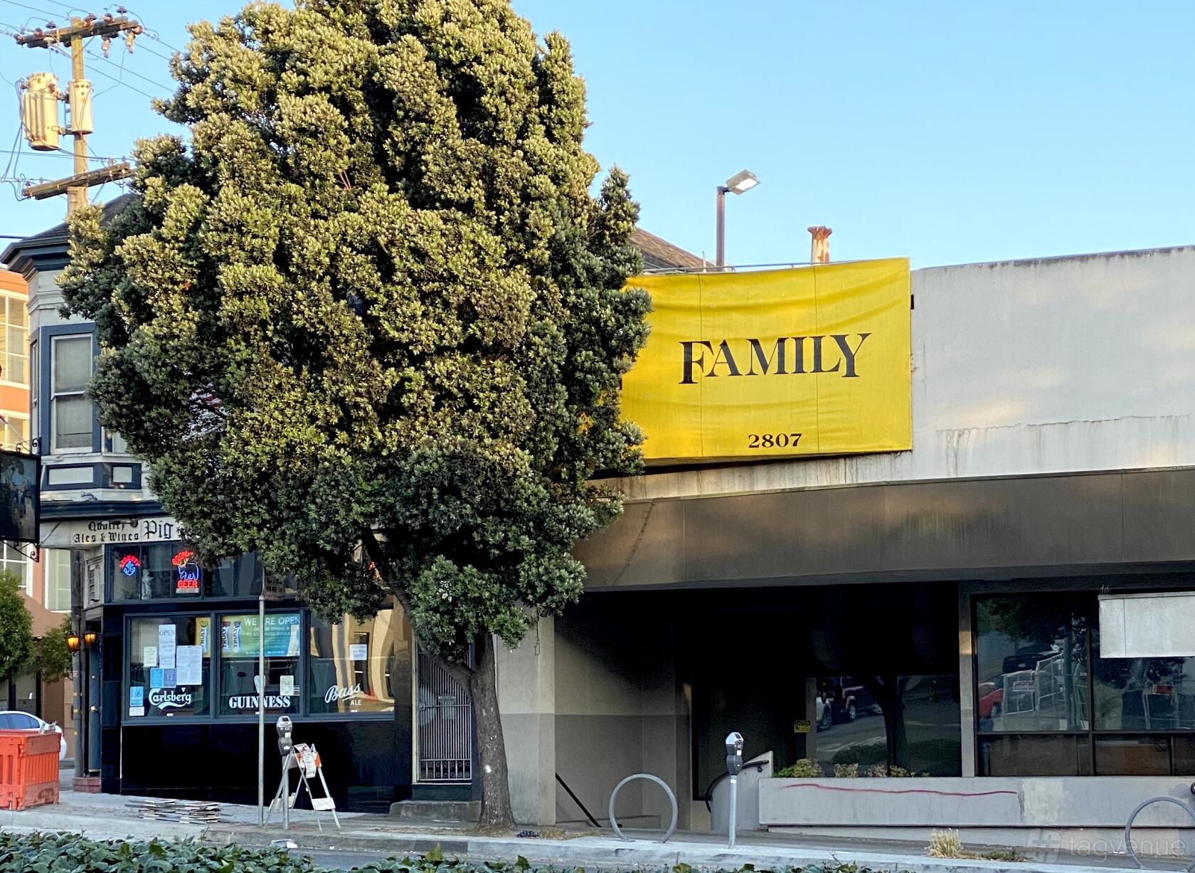 A corner pub with a large yellow 'Family' sign, tree out front, and glass entrance at Family Billiards.