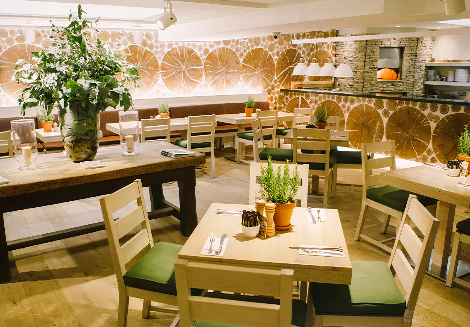 A cafe with wood tables, green cushioned chairs, potted herbs, and wall art resembling tree rings at Daylesford Organic Notting Hill.