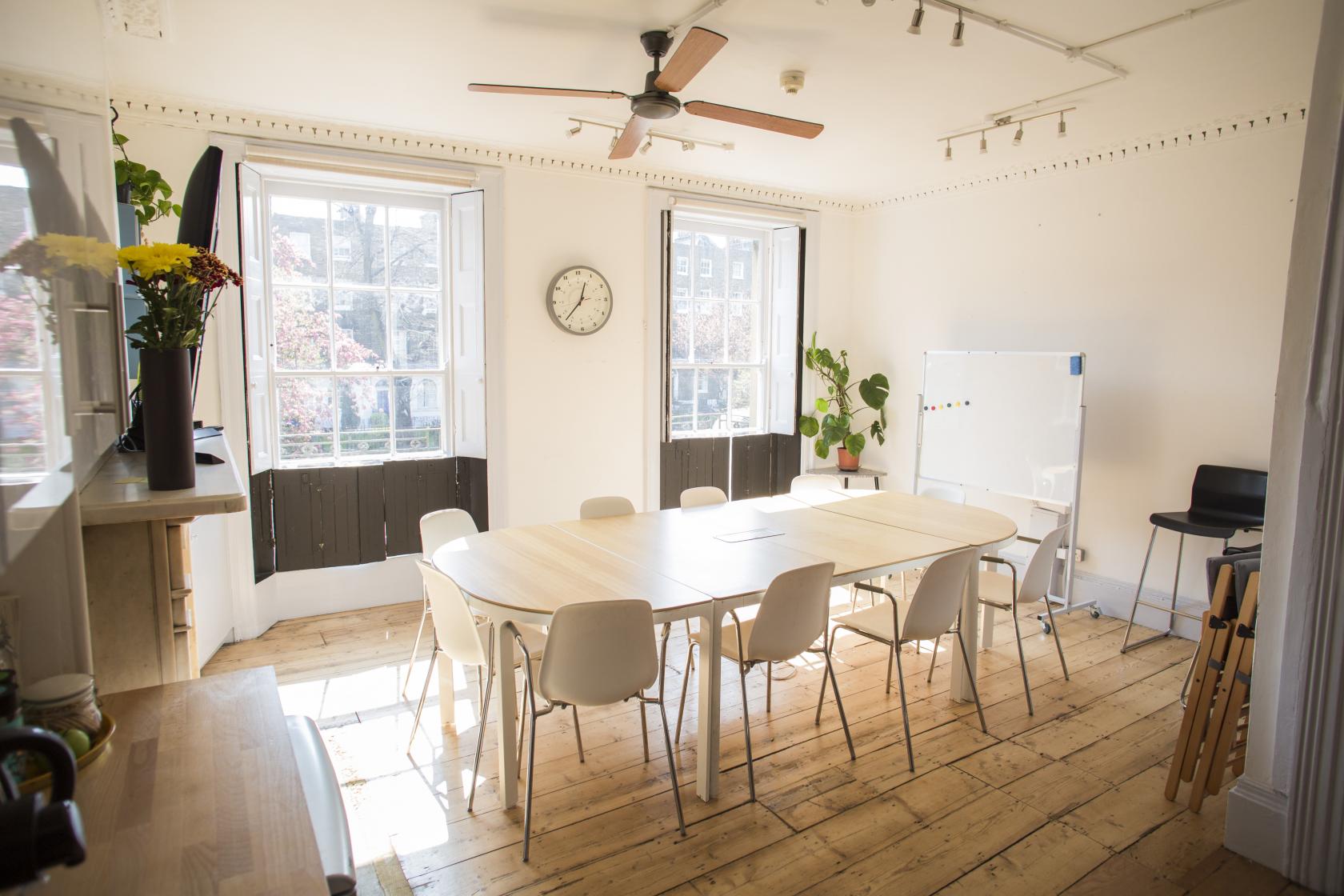 A meeting room with large windows, a central oval table with white chairs, plants, and a whiteboard at Anomalous Space.