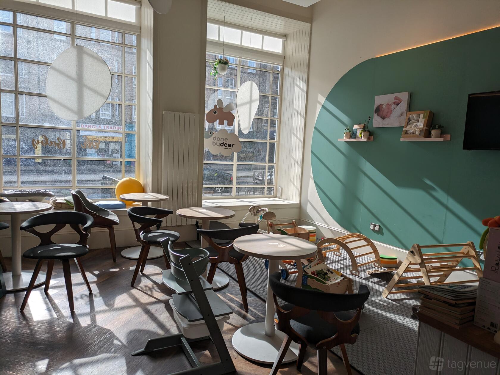 An event space in a cafe with large windows, round tables, wooden chairs, and a play area at Little Plaza.