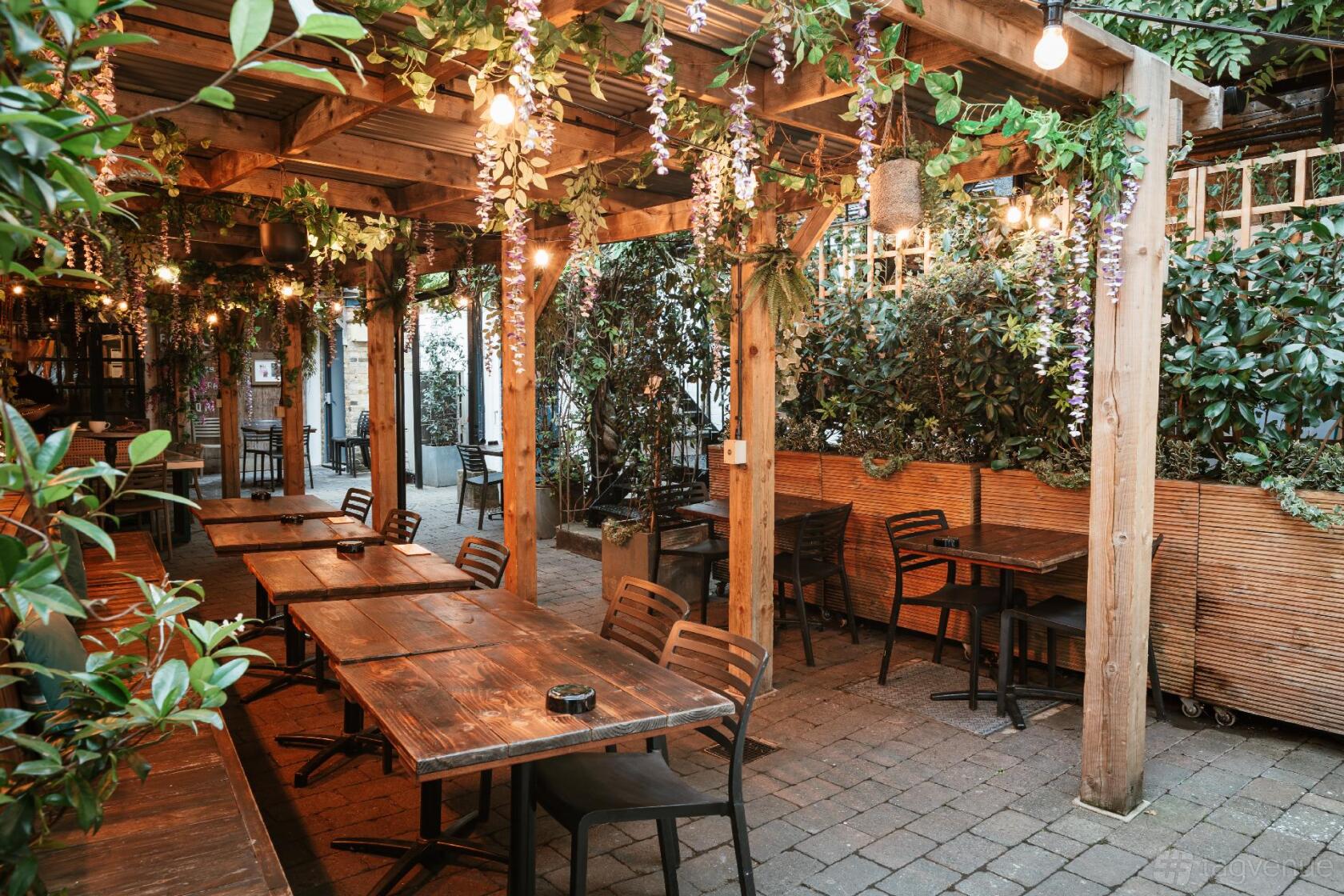 An event space with wooden pergola, hanging string lights, and greenery-covered walls at The George IV.