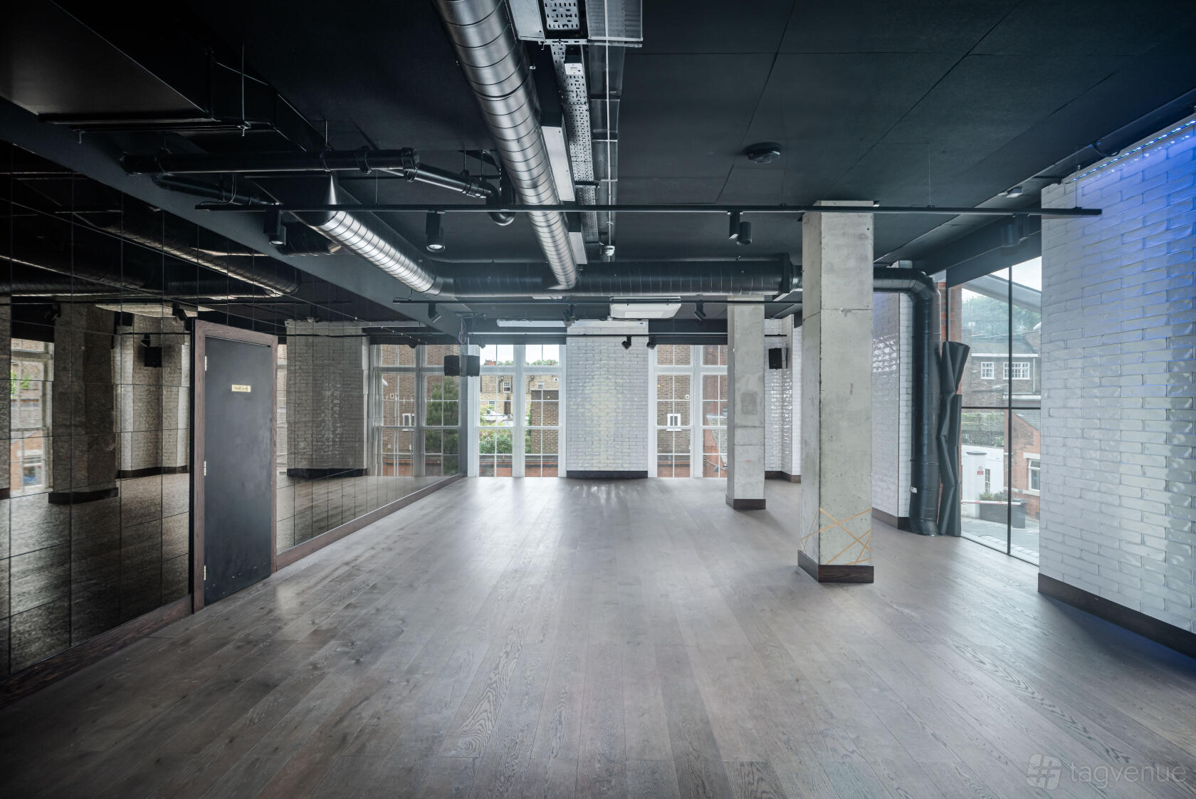 A meeting centre with exposed ductwork, floor-to-ceiling windows, and white brick walls at OMNOM.