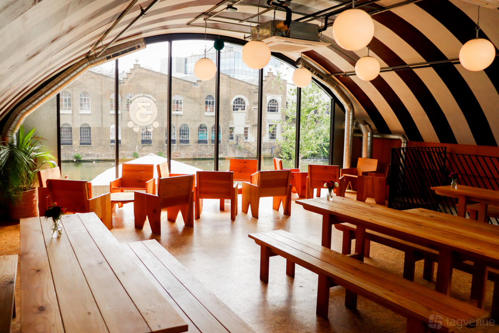 A function room with striped barrel ceiling, globe pendant lights, and wooden seating overlooking the river at 3Locks Industrial Brewery Riverside Views.
