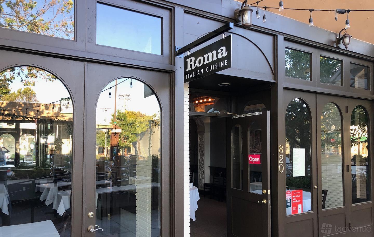 A restaurant entrance with arched windows, glass doors, and an outdoor string light at Roma.