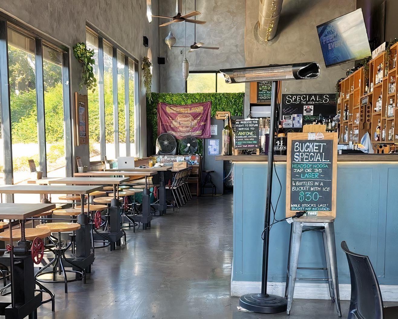 A bar with floor-to-ceiling windows, a chalkboard specials menu, and wooden tables at Craft Brew House.