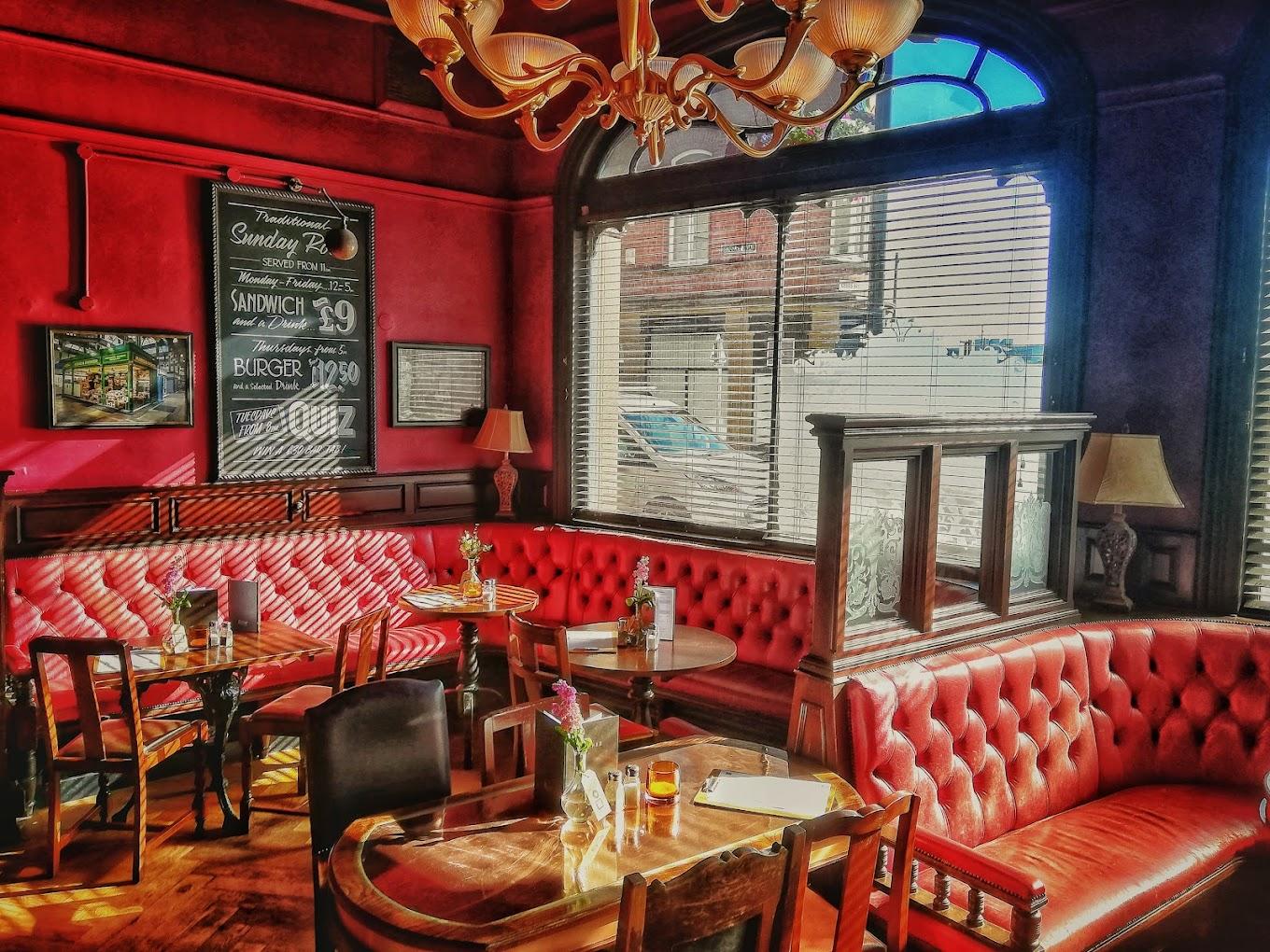 An event space in a pub with red tufted banquettes, wooden tables, and large windows at The Adelphi Pub & Restaurant.