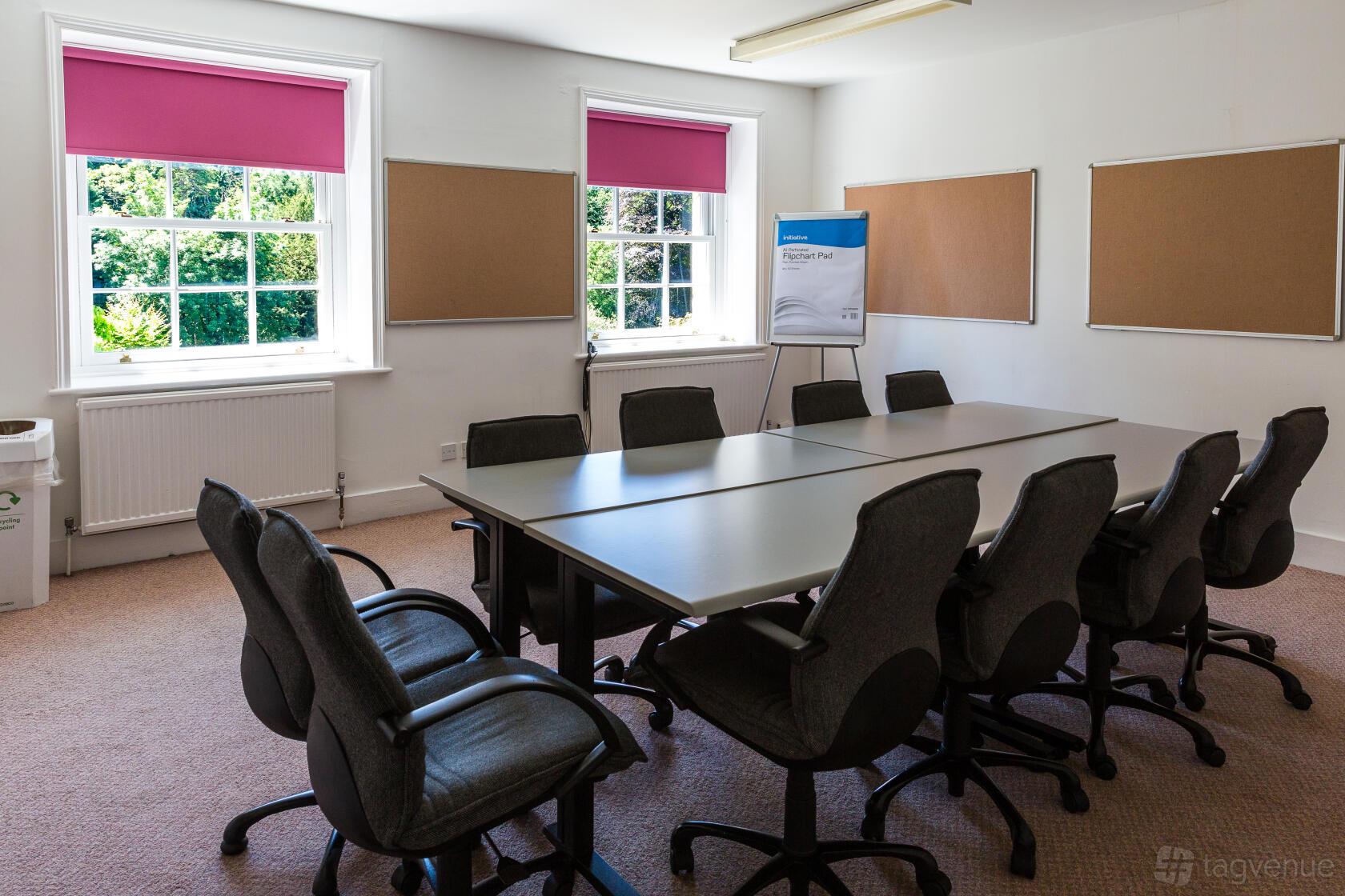 A meeting room with a rectangular table, cushioned chairs, cork boards, and large windows at Middle Aston House.