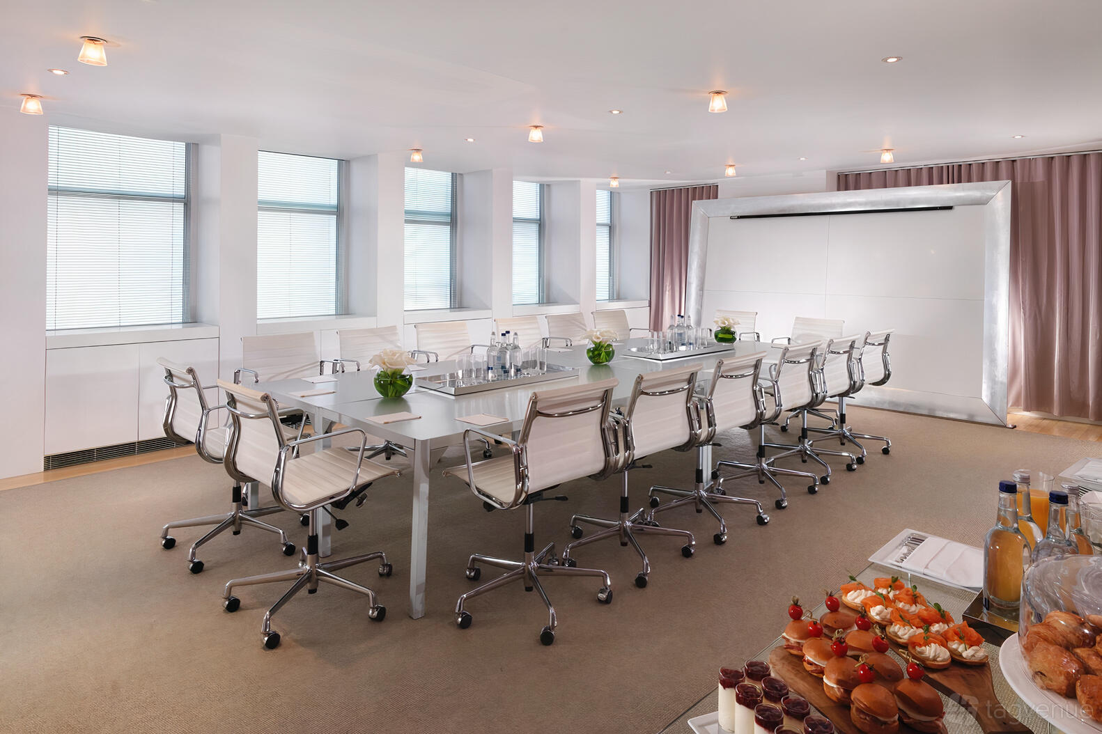 A boardroom with a large rectangular table, white rolling chairs, floor-to-ceiling windows, and refreshments at Sanderson London.