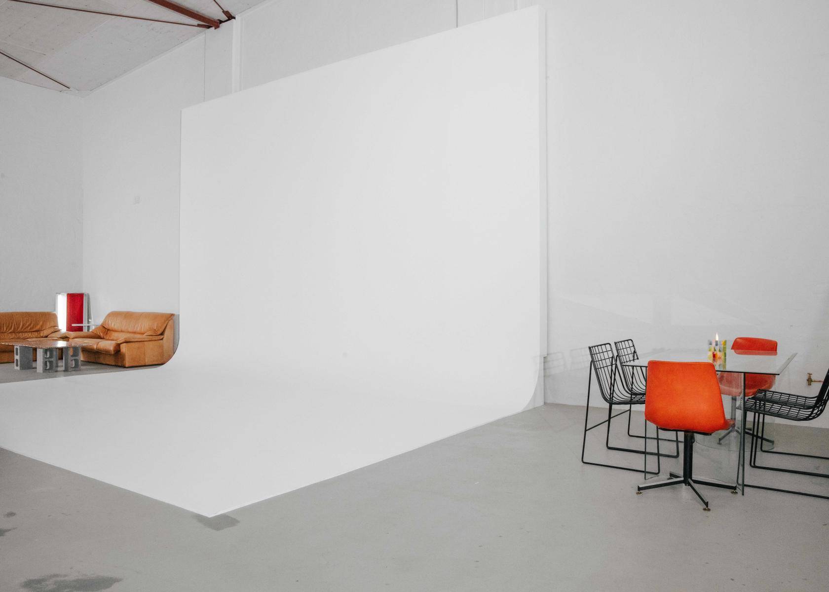 A photo studio with a large white cyclorama wall, leather sofas, and an orange dining set at UNO STUDIOS.
