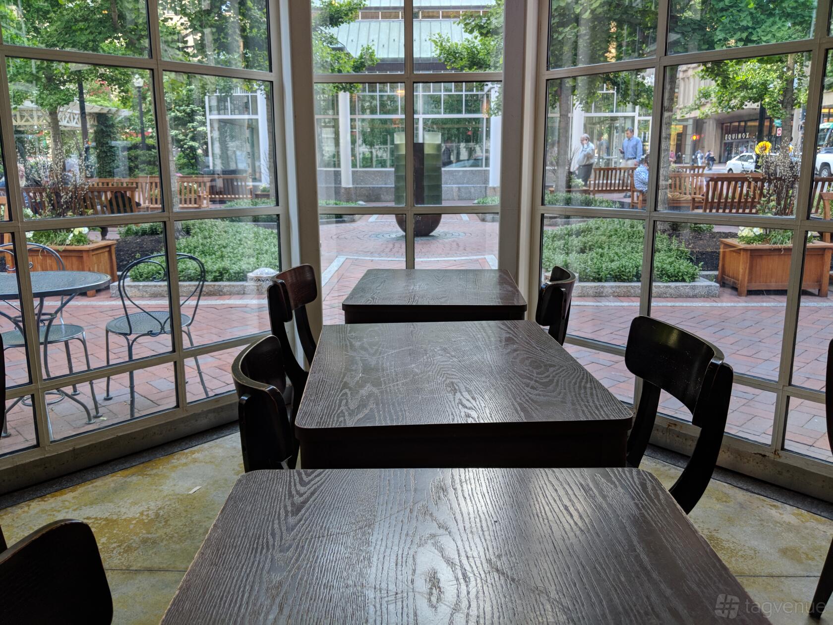 A cafe with wooden tables, black chairs, and large curved windows overlooking a brick patio at Sip Café.