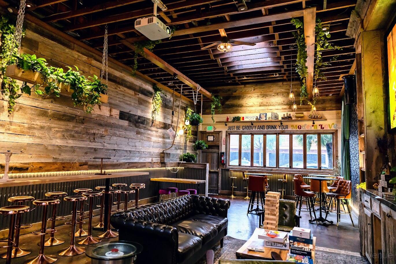 An event space in a bar with rustic wood walls, exposed beams, hanging plants, and a leather sofa at The Collective.
