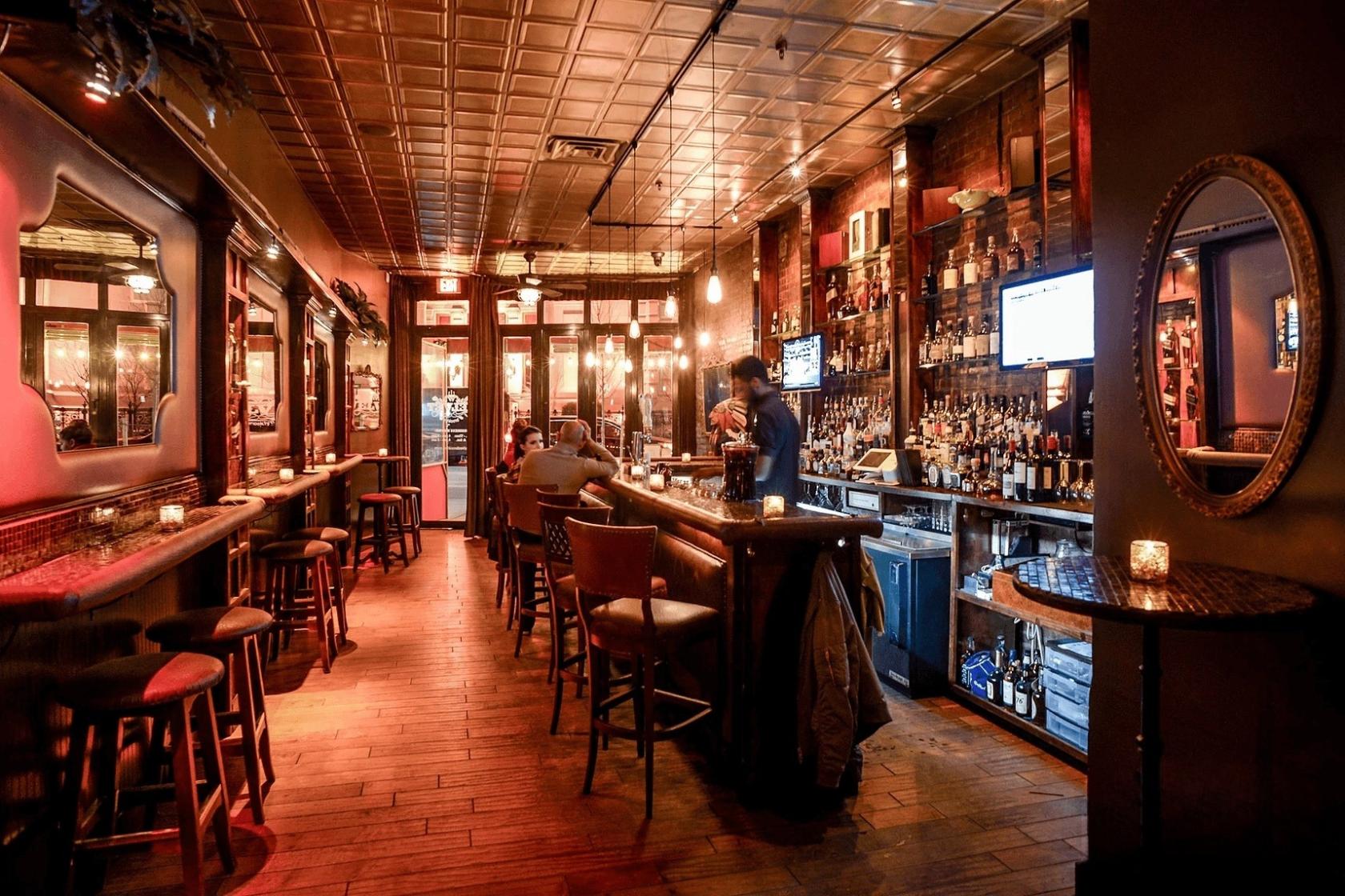 A bar with exposed brick walls, candlelit high tables, and a stocked bar area at Velvet Brooklyn.