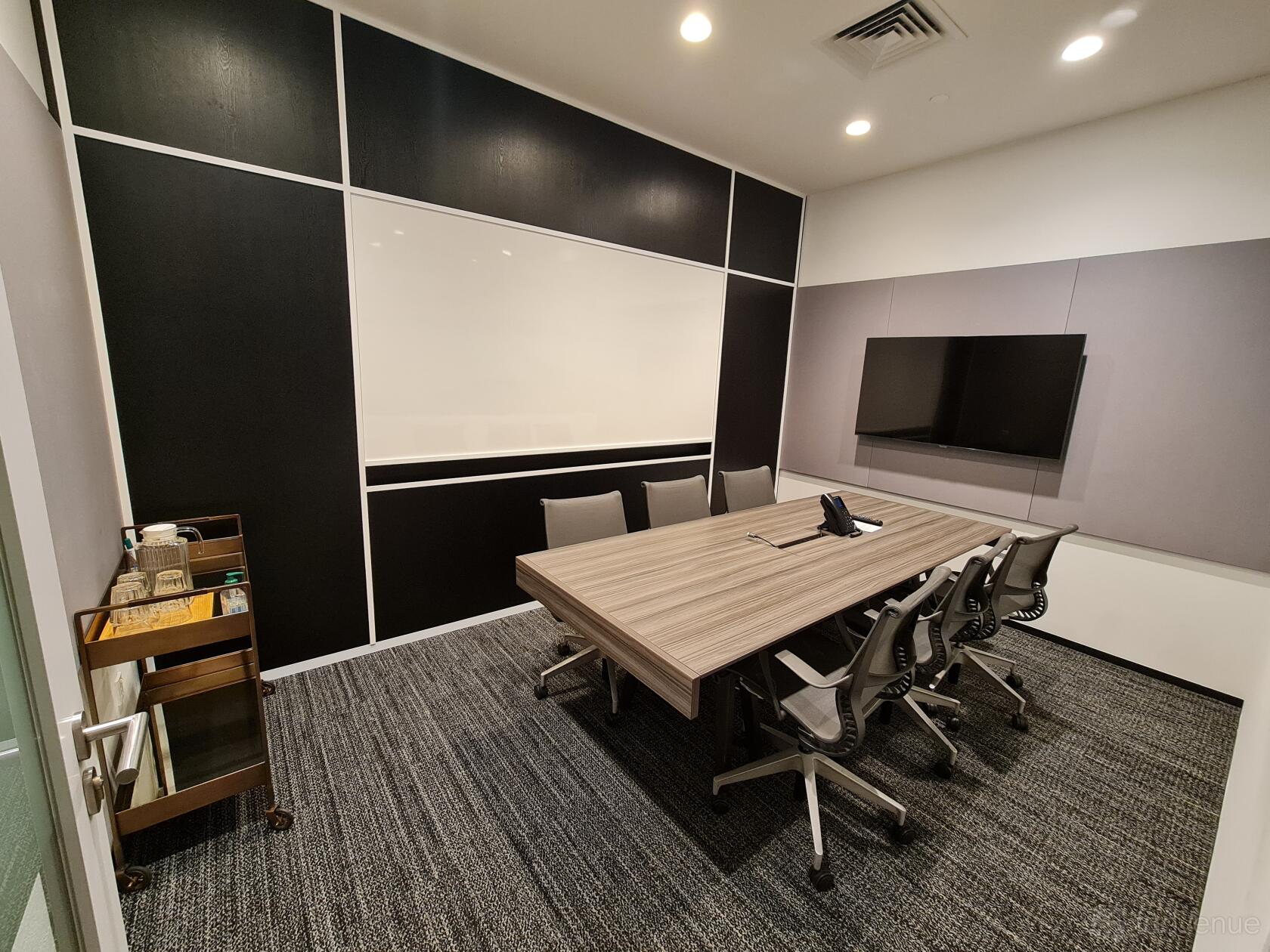 A coworking space with a rectangular meeting table, office chairs, wall-mounted screen, and glass door at The Work Project OUE Downtown.