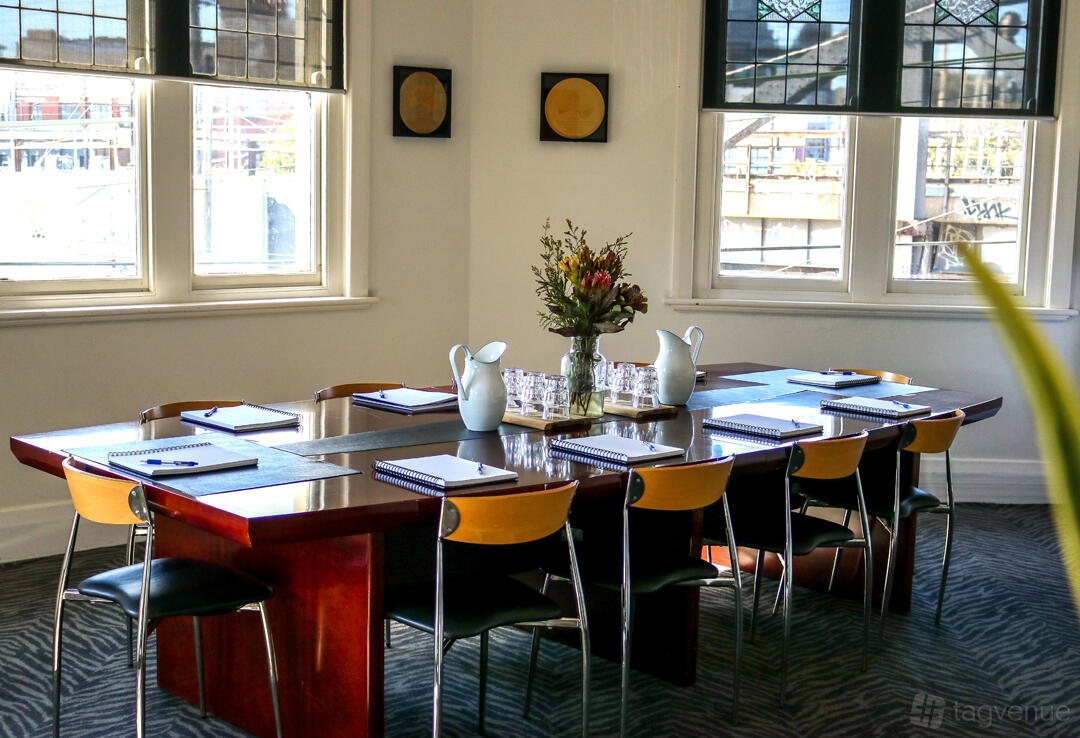 A boardroom with a polished wood table, notepads, pitchers, and large windows at The Precinct Hotel