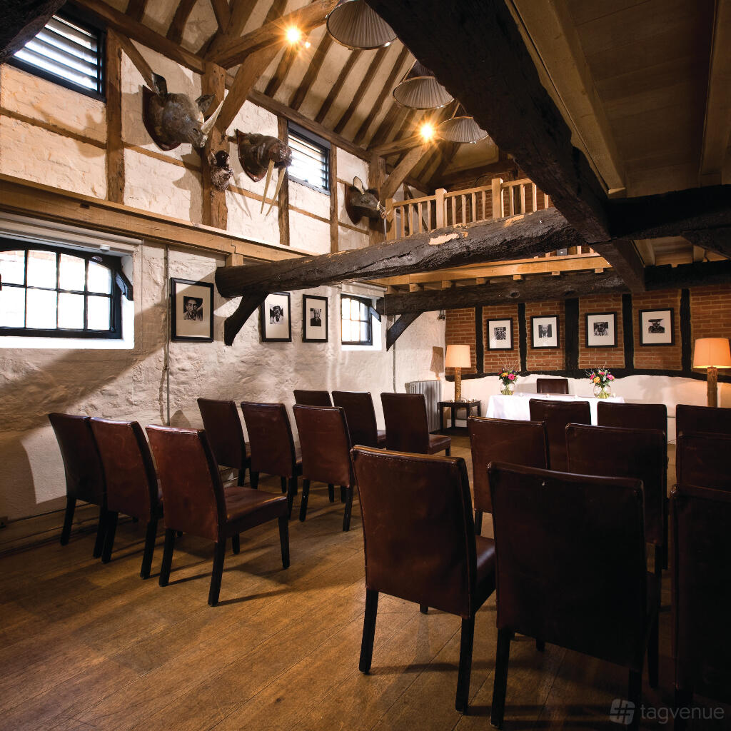 An event space with exposed beams, leather chairs, framed photographs, and rustic wood floors at Hotel du Vin Henley-on-Thames.