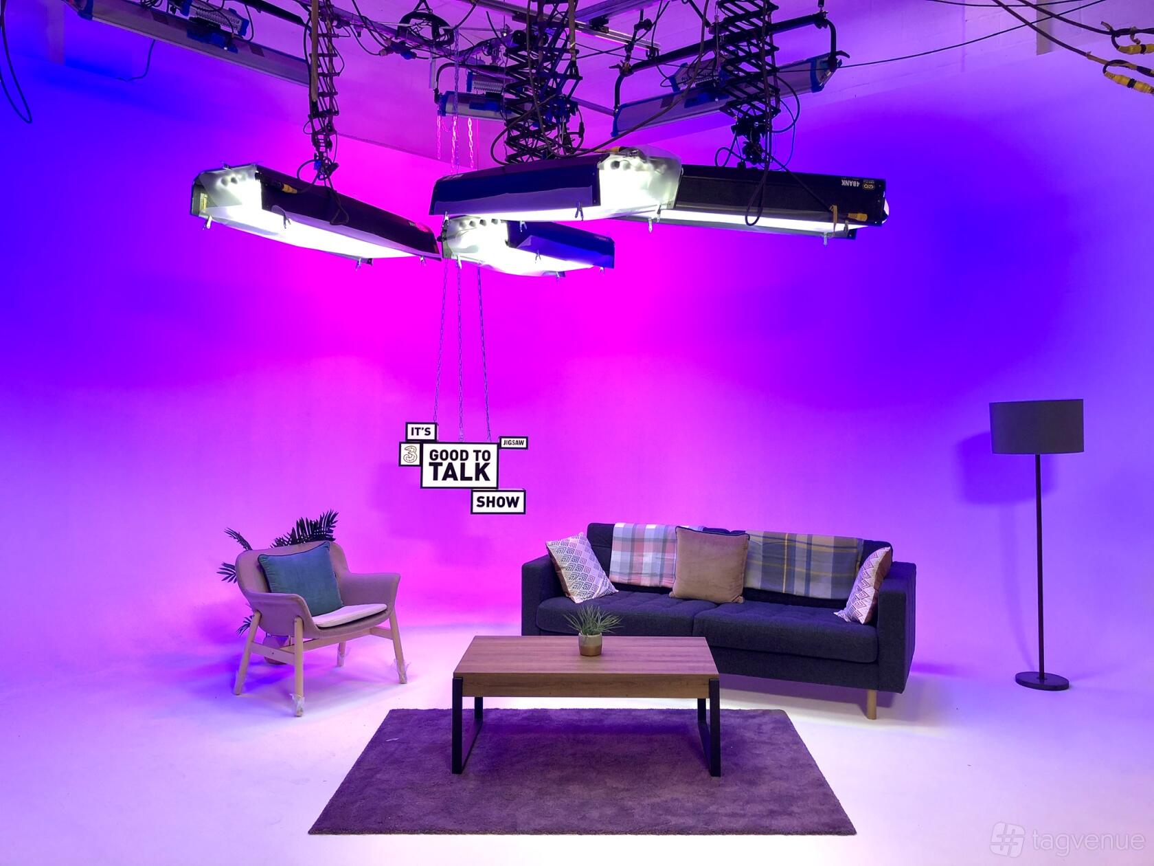 A film studio with purple lighting, a sofa, armchair, coffee table, and standing lamp at Studio 14.