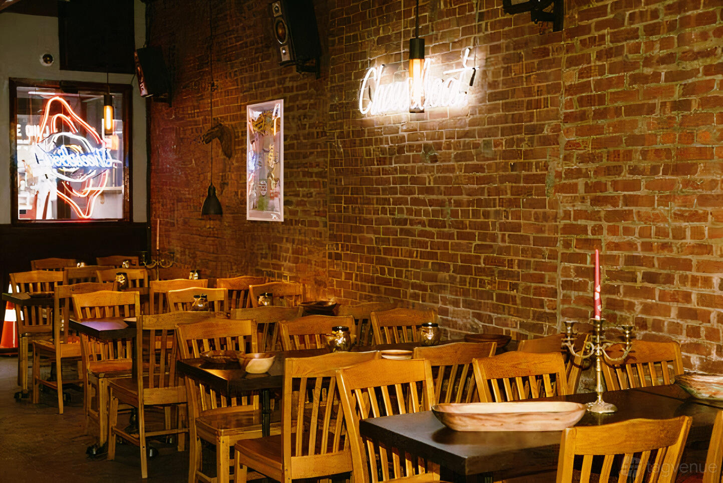 A restaurant with exposed brick walls, wooden tables and chairs, and neon signage at Cheeseboat Manhattan.