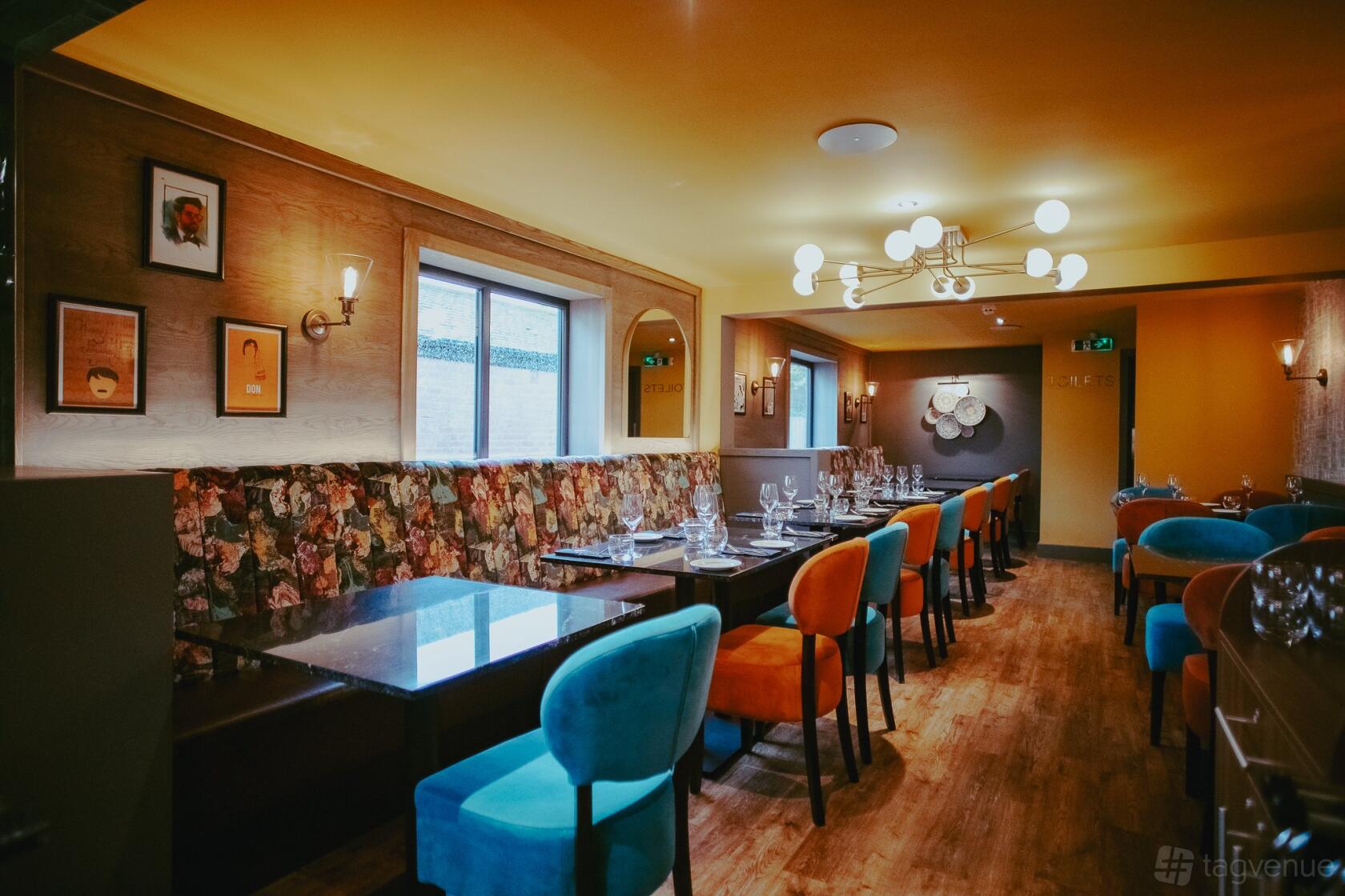 A restaurant with colorful velvet chairs, floral upholstered banquette seating, and modern light fixtures at Dastaan Leeds.