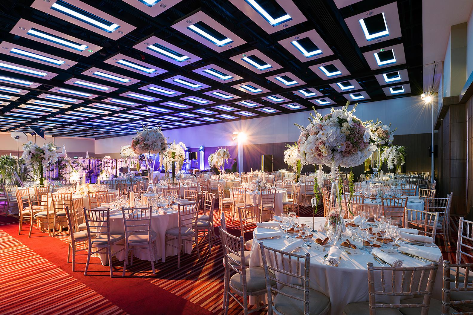 An event space in a hotel with round tables, silver chairs, and floral centerpieces at Mercure London Earl's Court.
