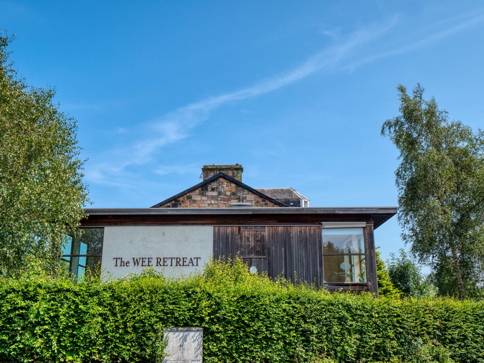 A dance studio with large windows, natural wood exterior, and leafy hedge at The Wee Retreat.