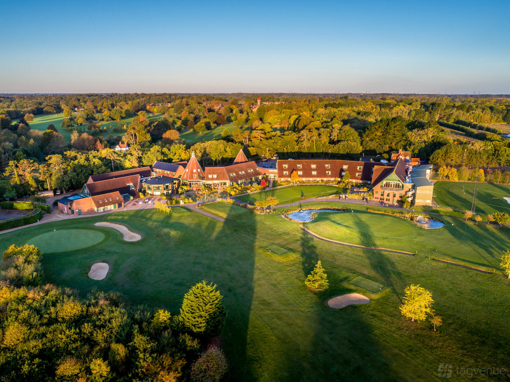 A hotel with sloped roofs surrounded by landscaped golf greens and water features at Ufford Park Woodbridge.