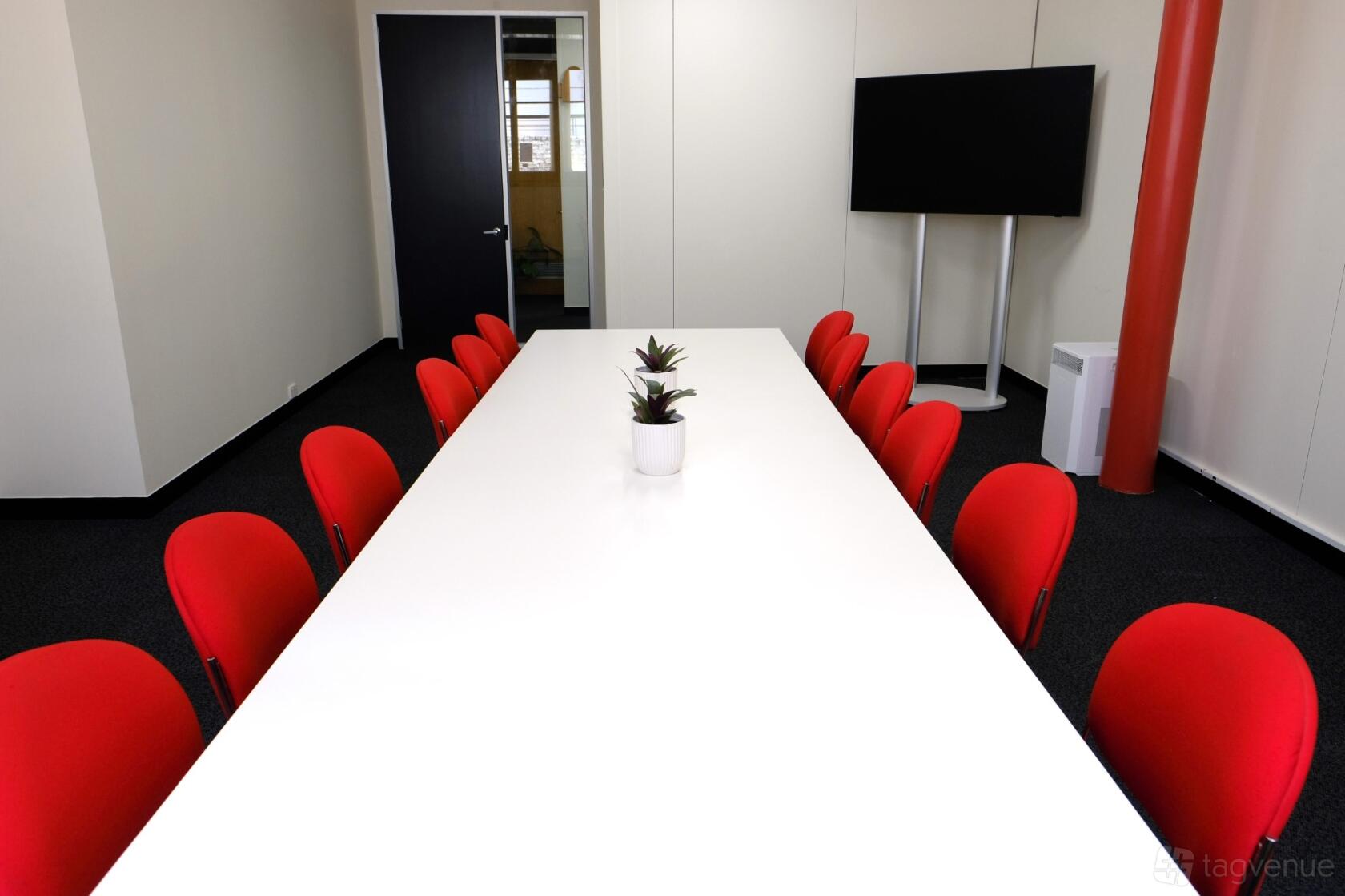 A meeting room with red chairs around a long white table and a wall-mounted TV screen at Ross House.