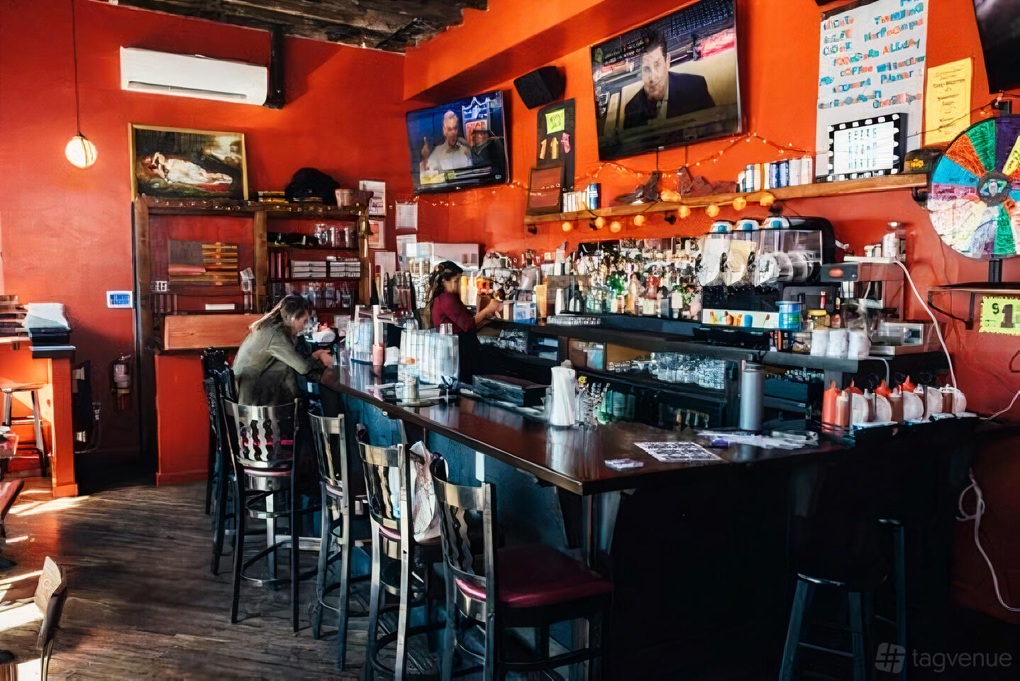 A cozy bar with red walls, wooden floors, high chairs, and a stocked counter under wall-mounted TVs at Echo Bravo.