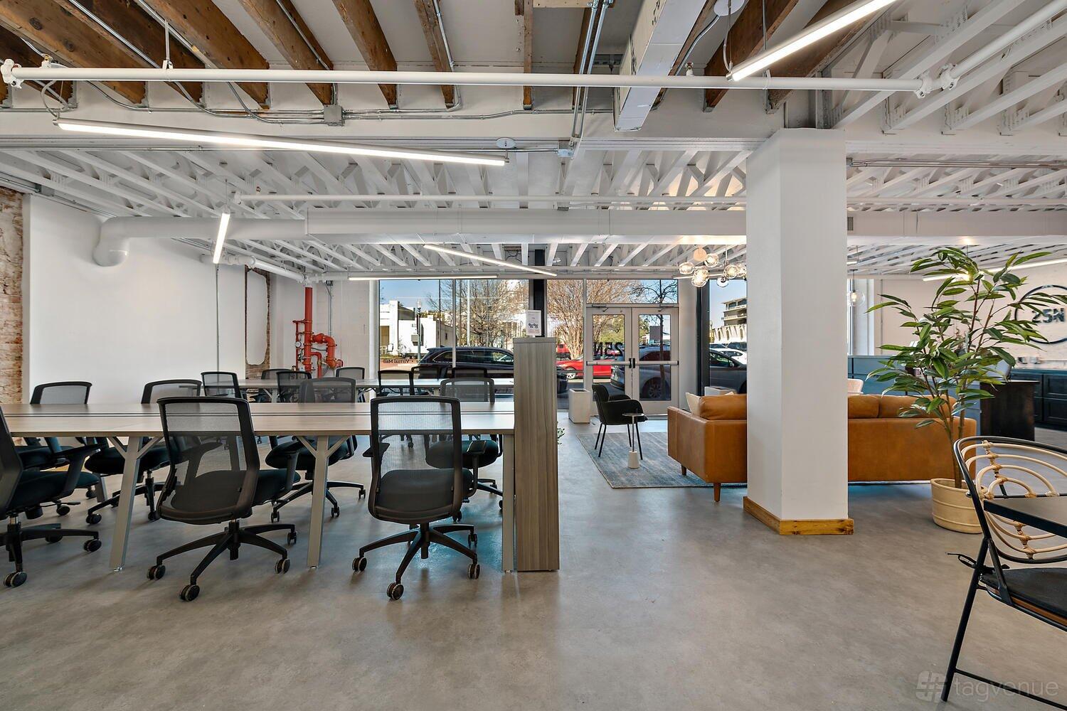 An event space with exposed wood ceilings, long work tables, rolling chairs, and a lounge area at 25N Coworking Waco.