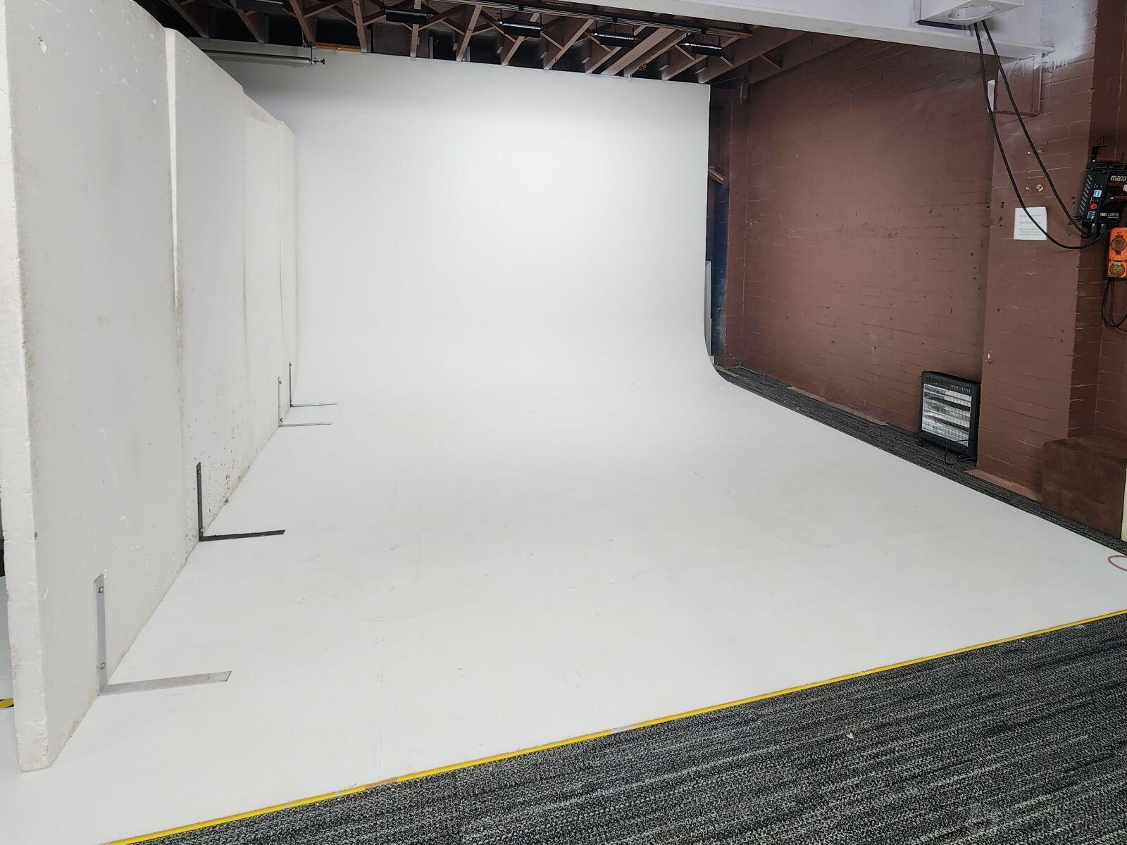 A photo studio with a white cyclorama wall, concrete flooring, and exposed ceiling beams at Dragon Image Sydney Studios.