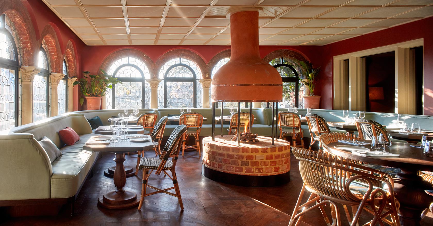 A restaurant with arched windows, a central brick fireplace, and rattan chairs at Belvedere.
