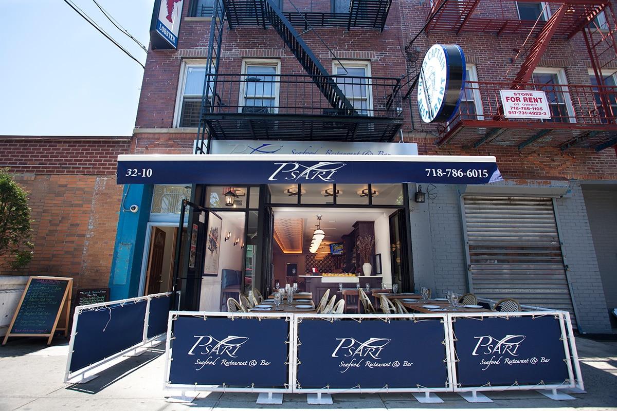 A restaurant terrace with outdoor seating, blue barriers, and an open facade at Psari Restaurant.