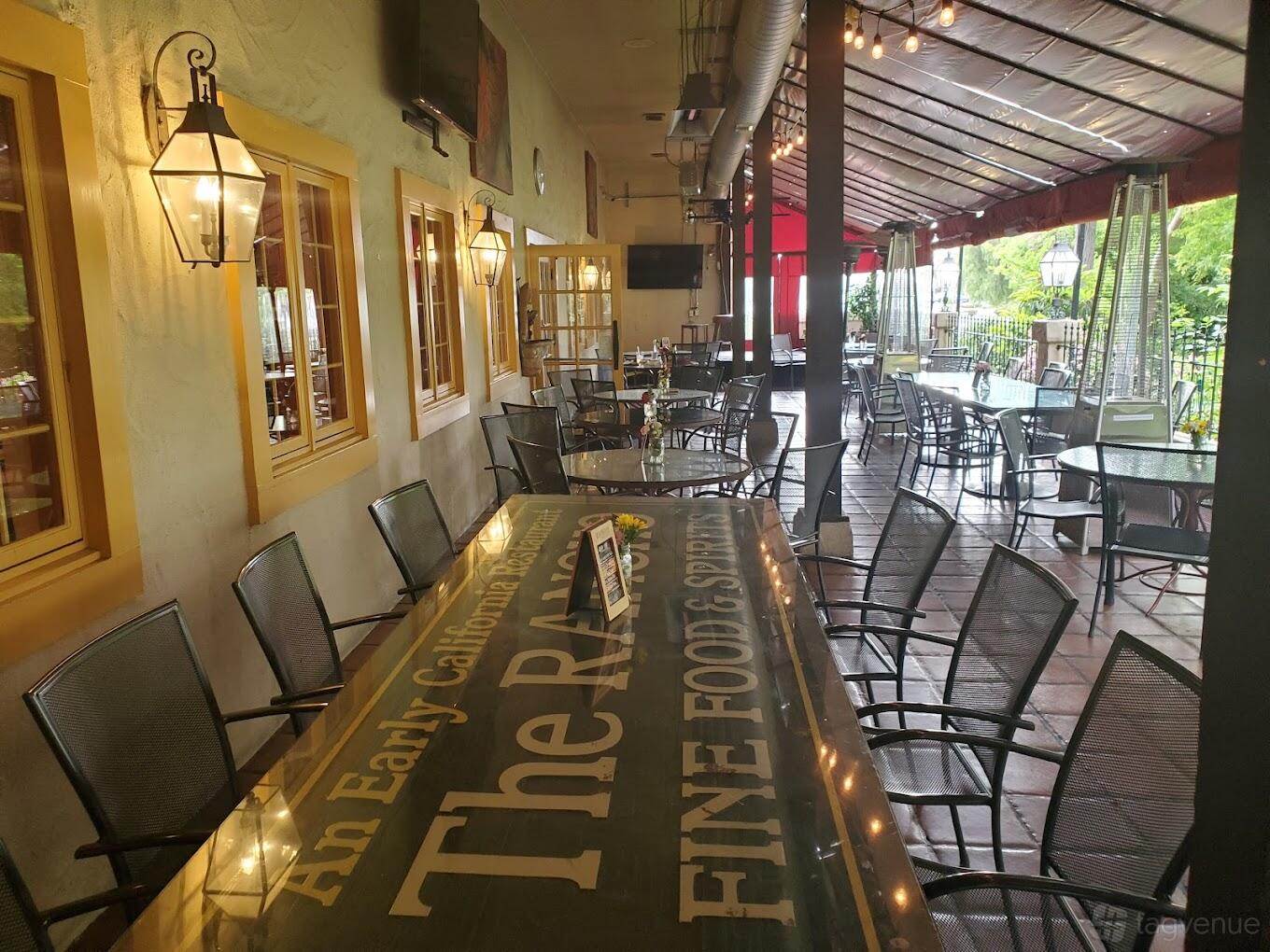 A terrace with metal chairs, long tables, hanging lanterns, and a covered roof at WildWood Crossing and Cantina.