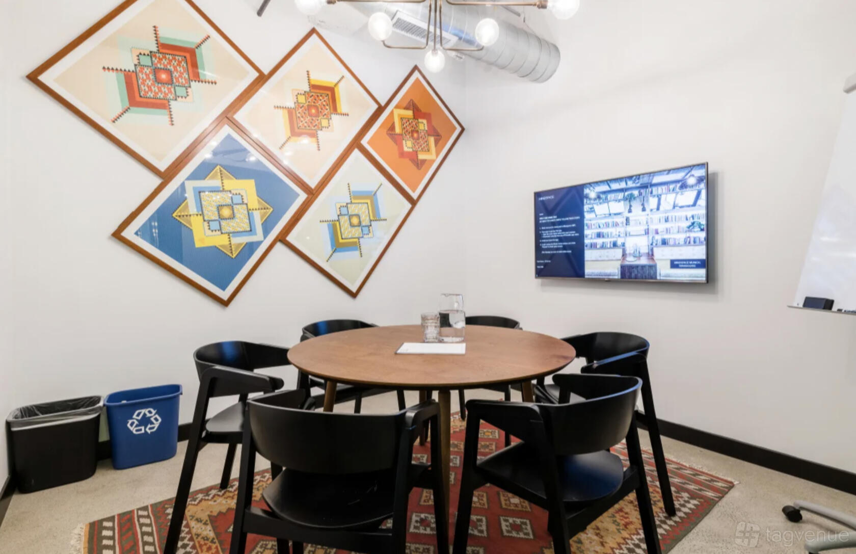 A meeting room with a round wooden table, black chairs, wall-mounted screen, and geometric art at Mindspace San Francisco.