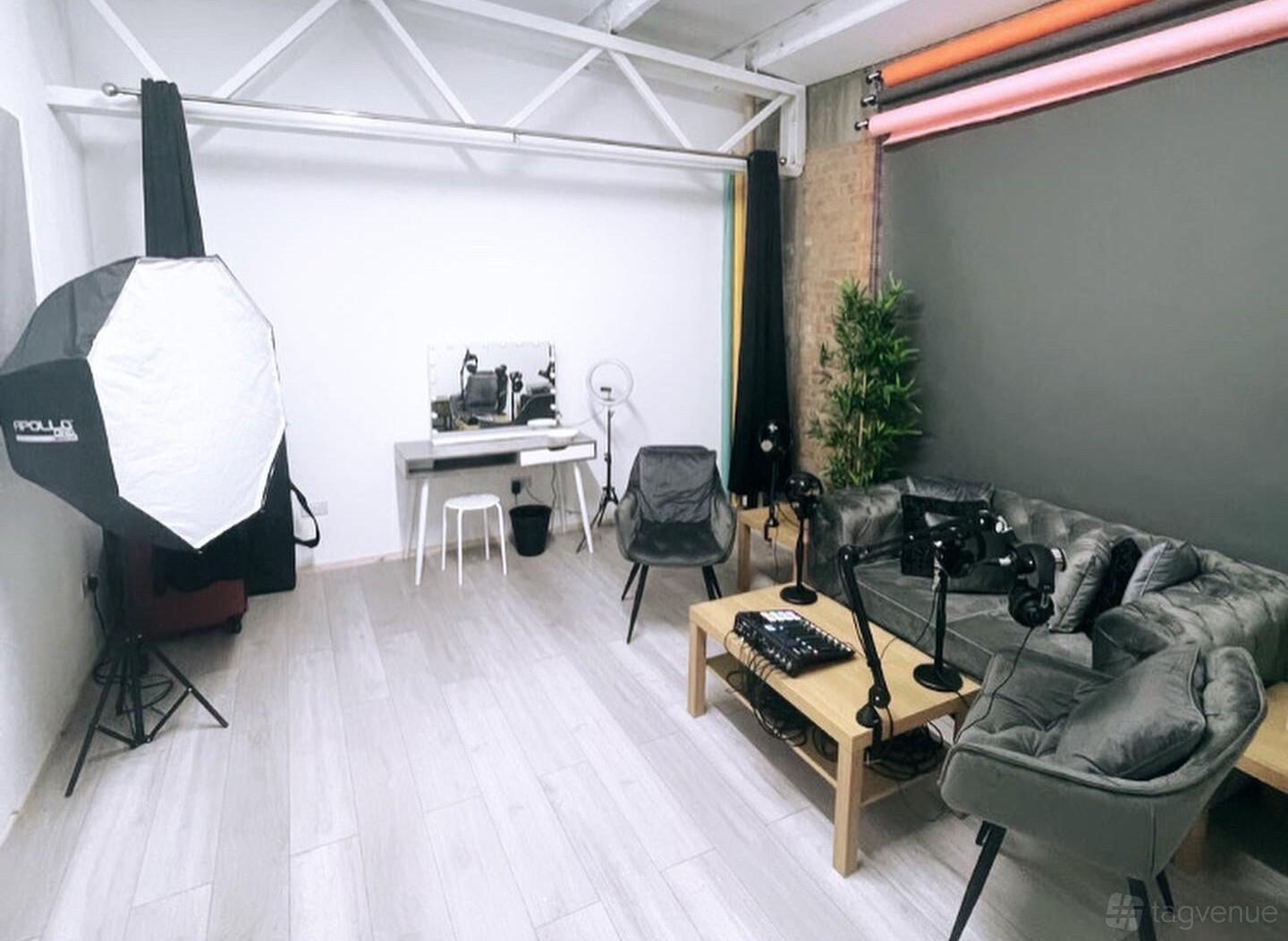 A podcast studio with a gray sectional sofa, microphones on a wooden table, and photography lighting at Creative Quarters.