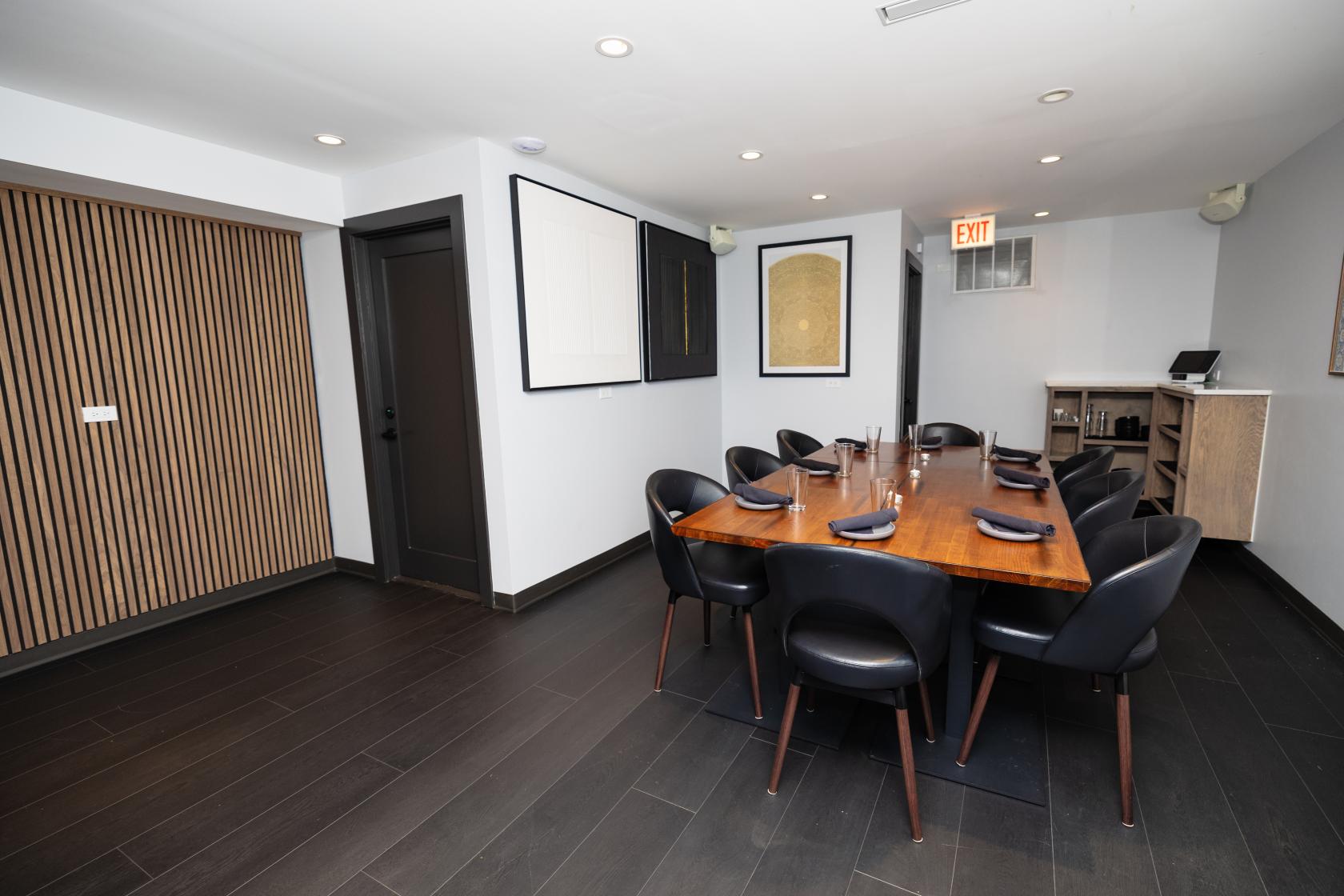 An event space in a restaurant with a wooden table, black chairs, and modern wall art at Tandoor Char House - Lincoln Park.