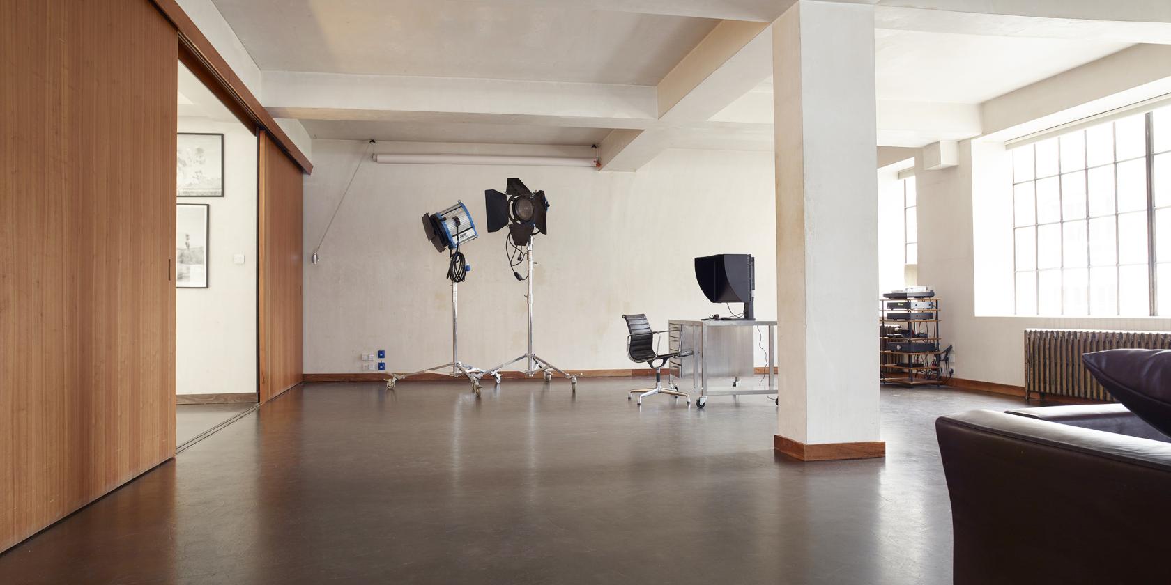 A photo studio with large overhead lights, a minimalist desk, and natural lighting at Roberts Place Studios.
