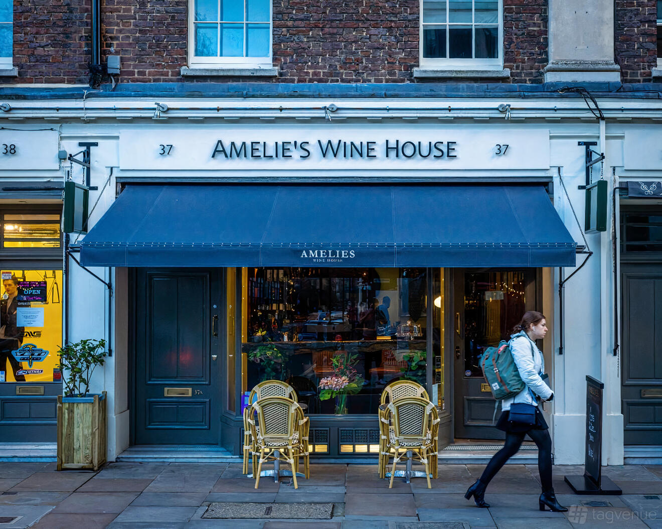 A pub with a navy awning, glass entrance, and two outdoor bistro chairs at Amelie's Wine House.