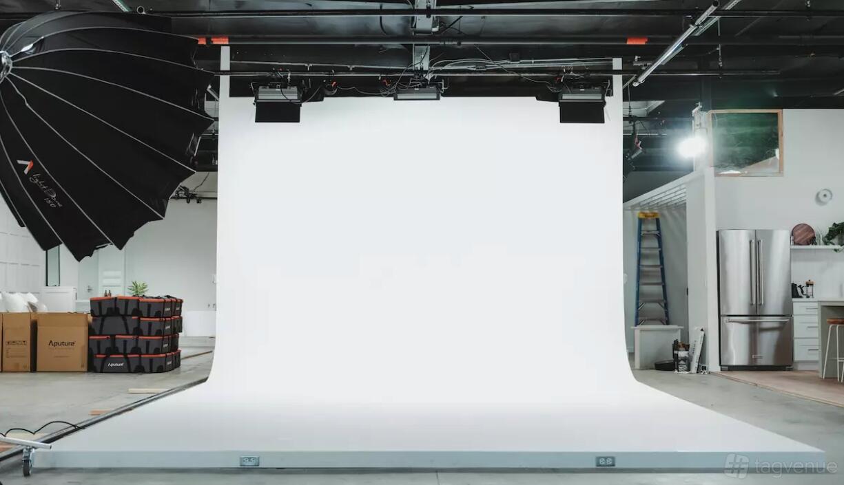 A photo studio with a large white cyclorama wall, overhead lighting, and a black umbrella reflector at Influence Studios - San Diego.