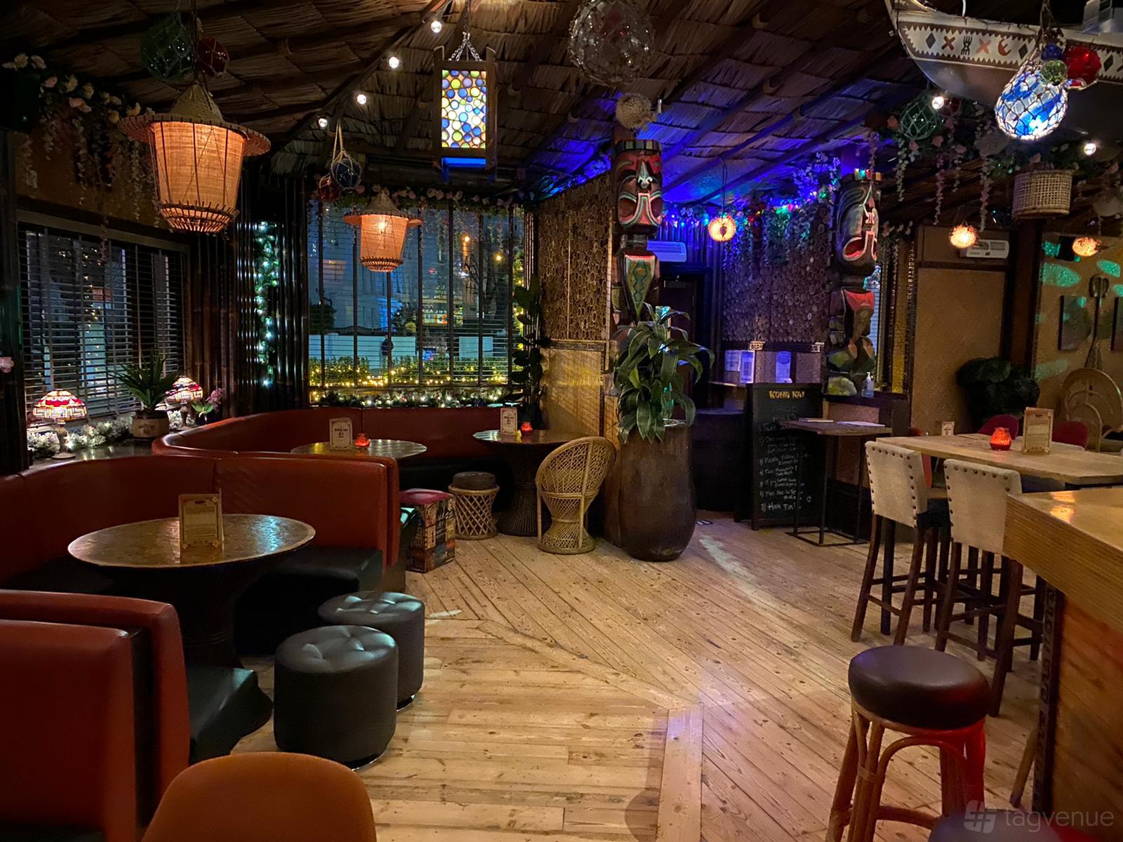 An event space in a cocktail bar with tropical decor, bamboo ceiling, lantern lighting, and round tables at Kona Kai.