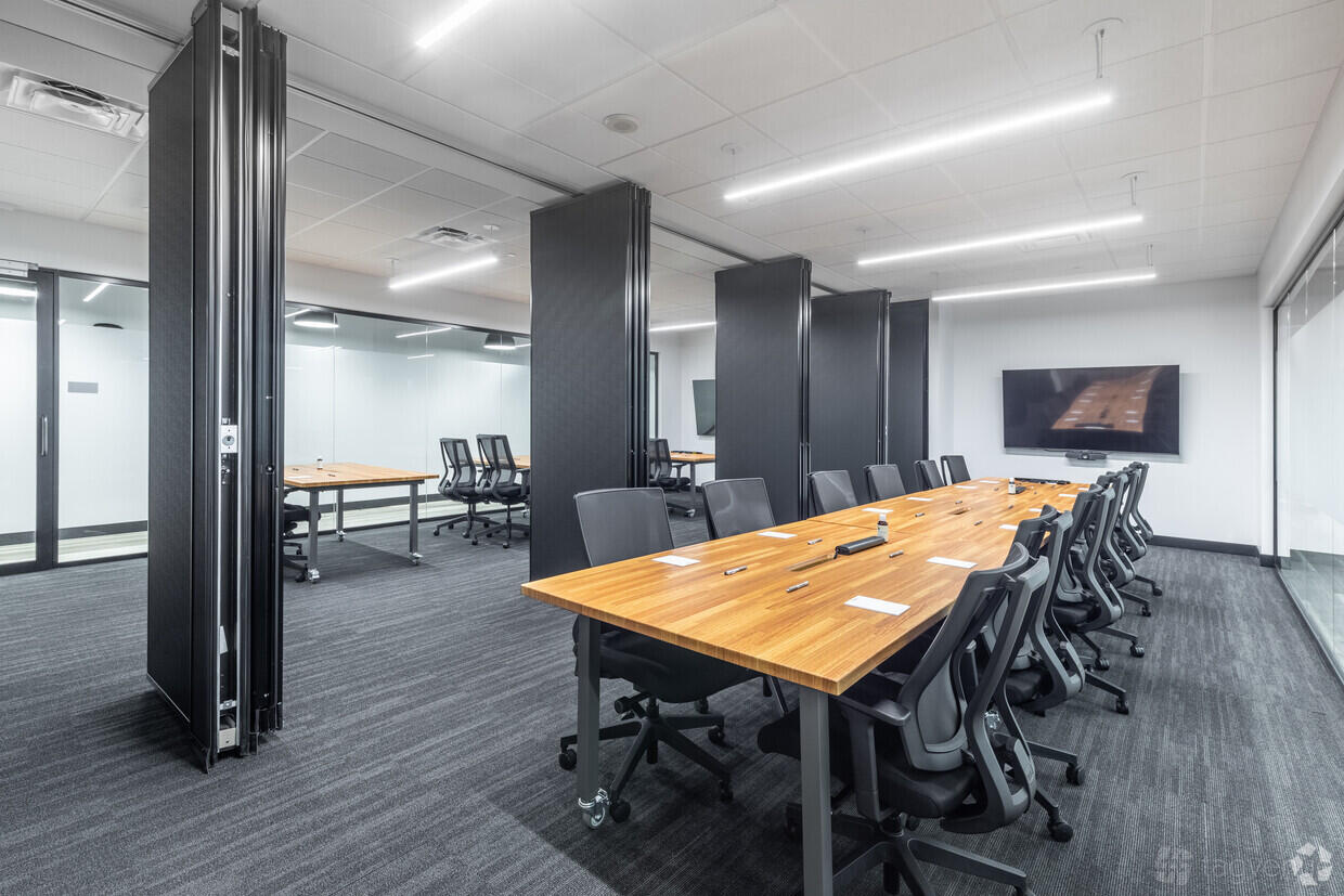 A meeting room with large wood conference tables, ergonomic chairs, and a wall-mounted screen at Venture X Arlington - Courthouse Metro.