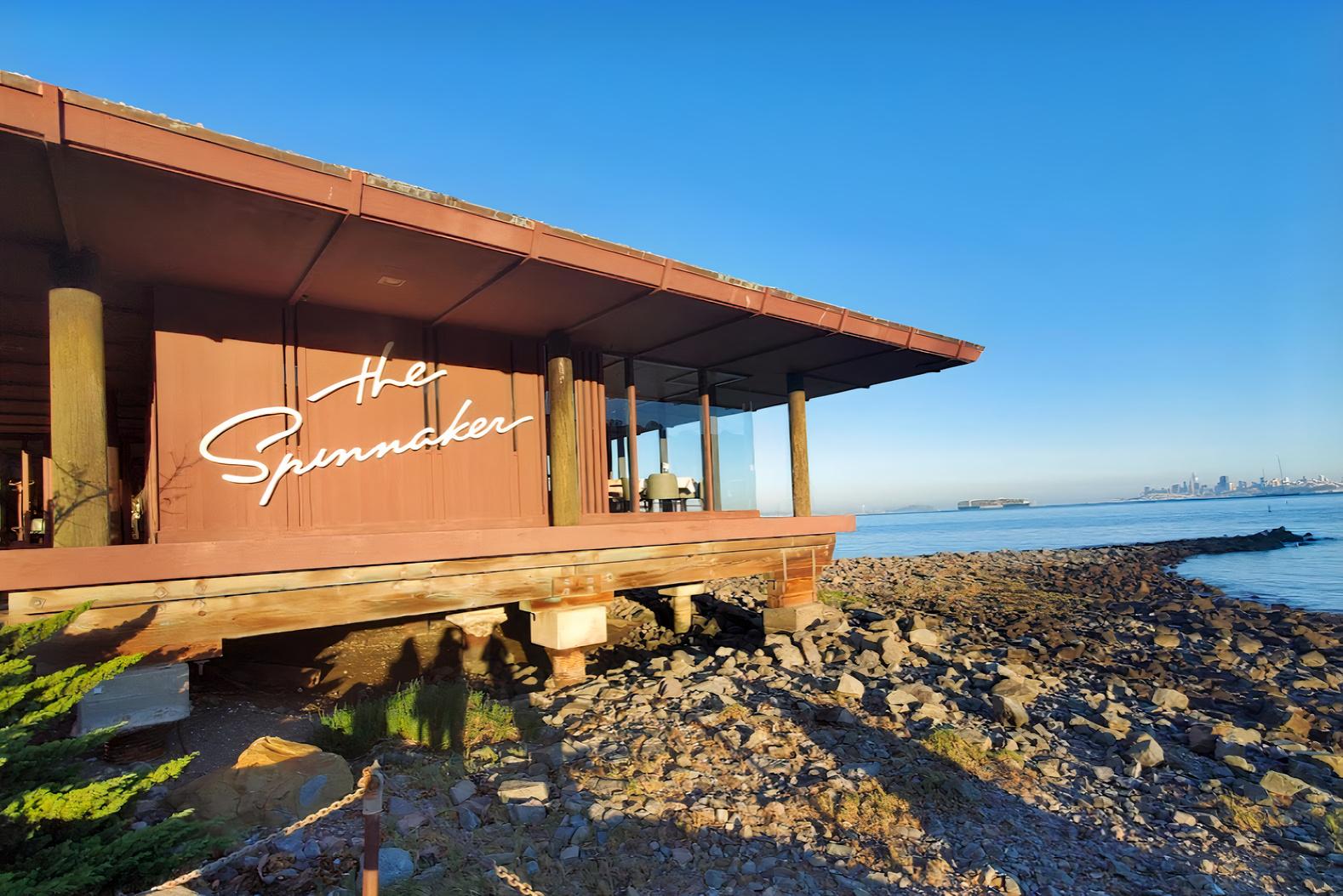 A waterfront restaurant with large windows and a sign reading 'The Spinnaker' overlooking rocky shoreline.