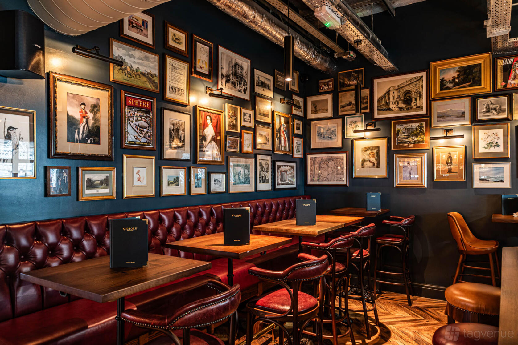An event space in a pub with tufted leather banquettes, wooden tables, and a gallery wall of framed art at Victory Pub & Kitchen.