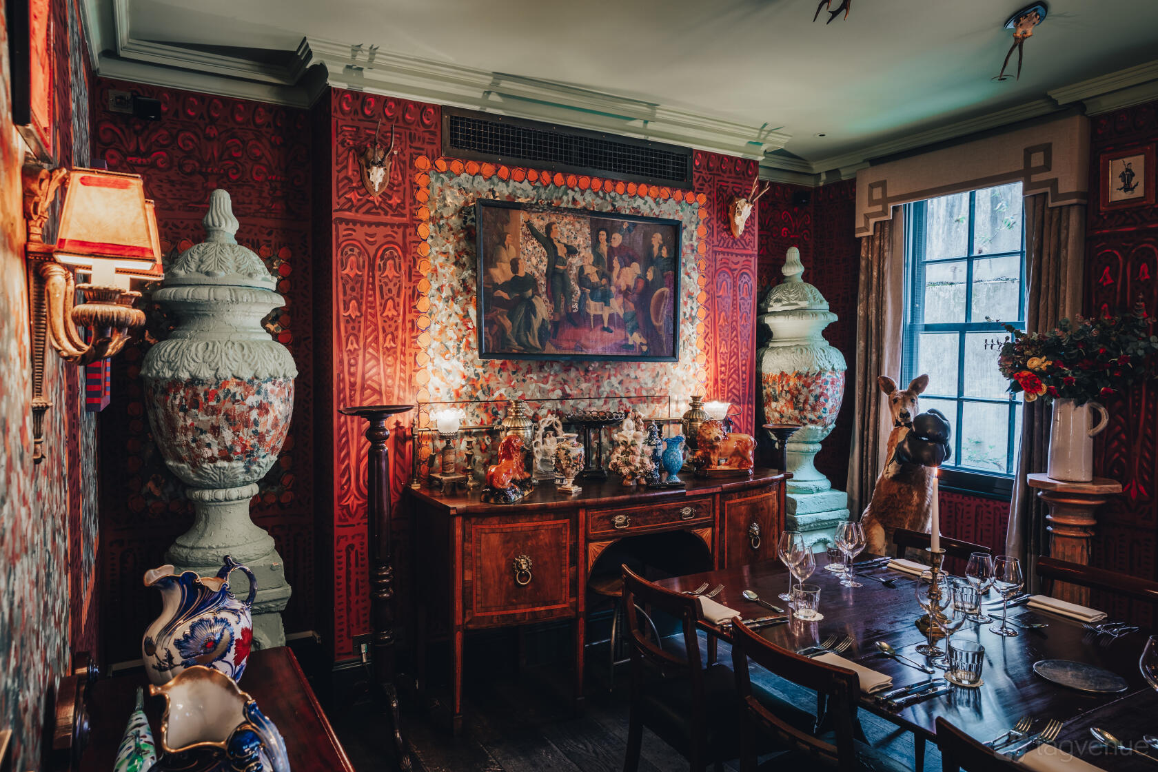 A hotel dining room with ornate red wallpaper, vintage decor, large urns, and a wooden table at The Zetter Clerkenwell.