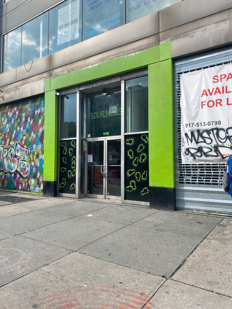 A warehouse with glass double doors, neon green trim, and graffiti on the facade at Sour Mouse.