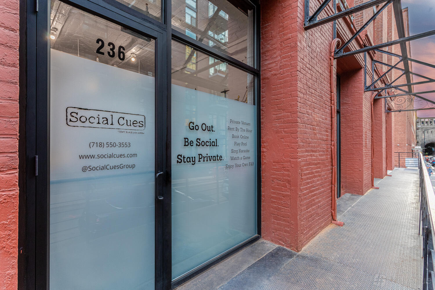 An event space entrance with frosted glass doors, black framing, and red brick facade at Social Cues - The Gallery.