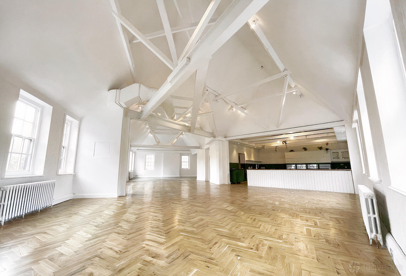 A photo studio with white walls, vaulted ceiling with exposed beams, large windows, and parquet flooring at B&H Studios.
