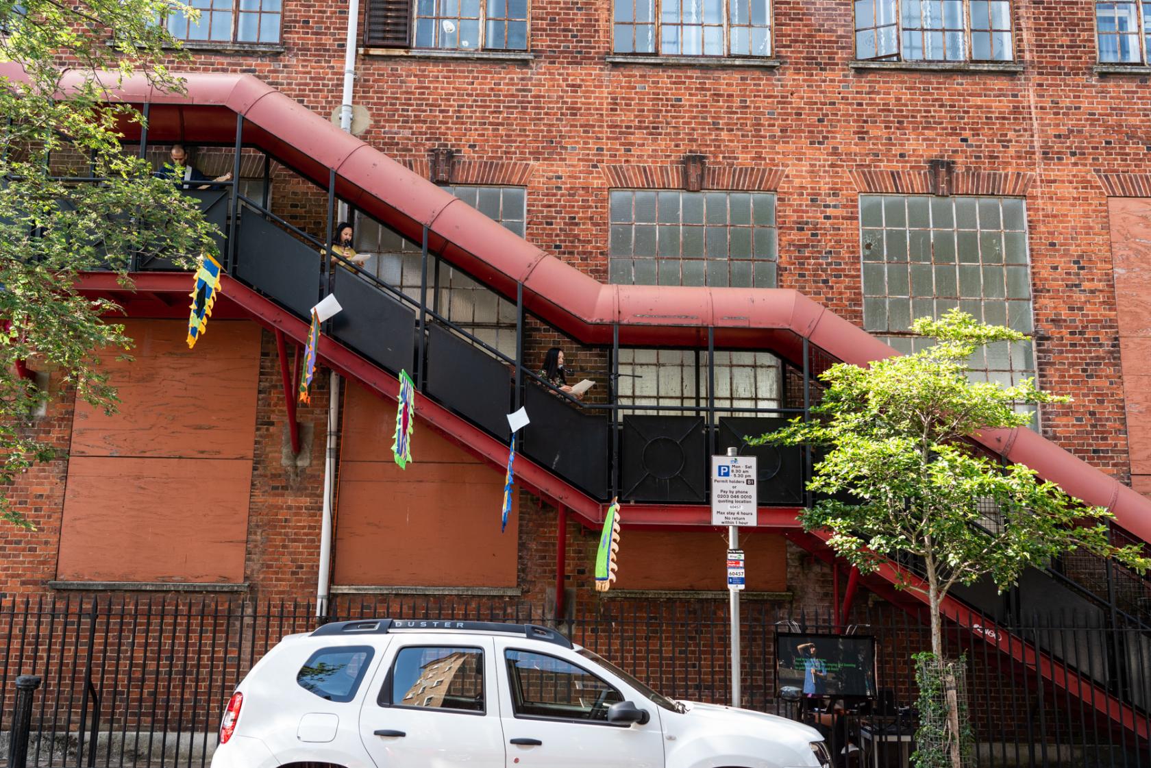 A brick building with large factory windows and a red metal staircase outside Chisenhale Dance Space.