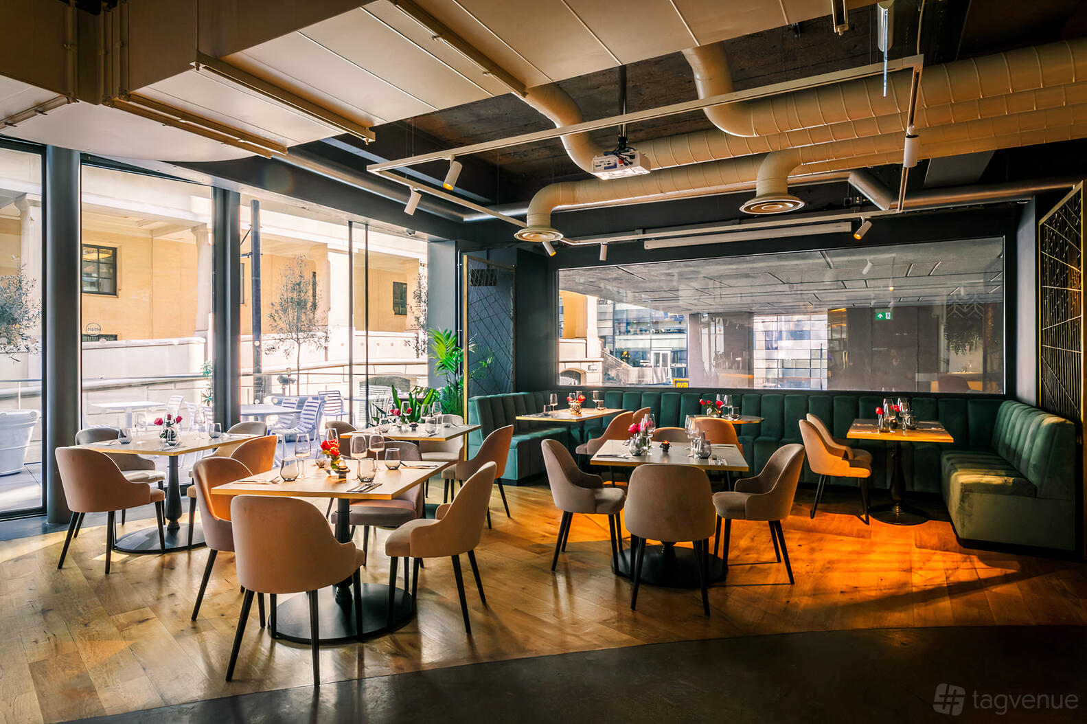 An event space in a cocktail bar with velvet banquettes, round tables, and floor-to-ceiling windows at The Listing.